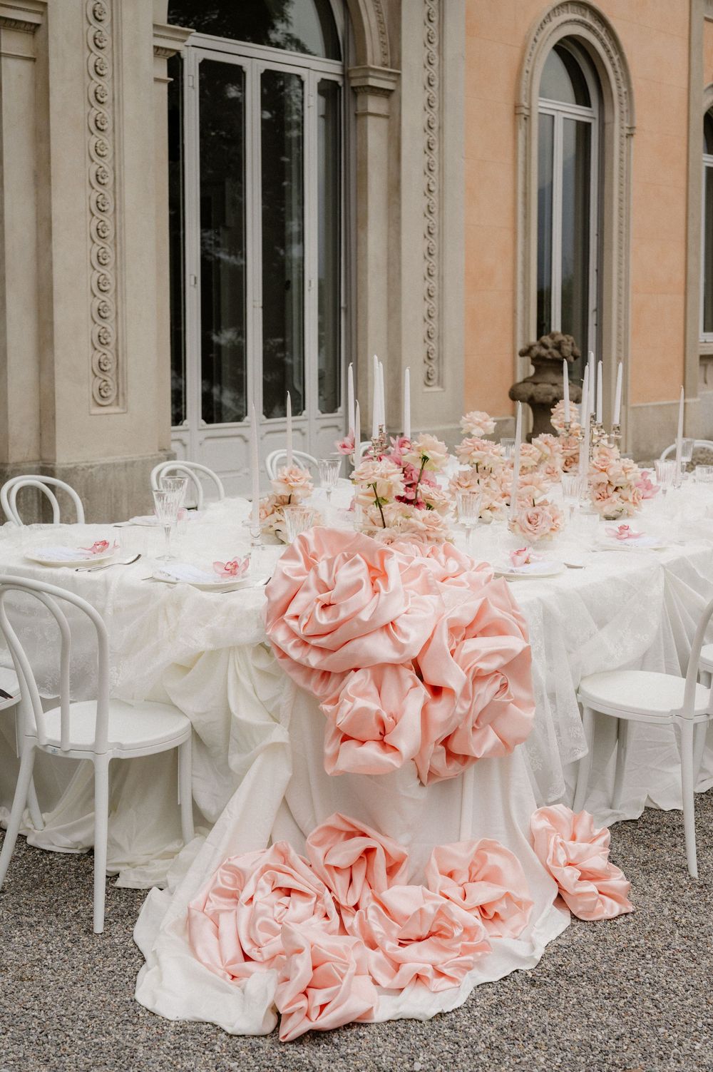 Elegant wedding table setting with pink floral decorations and white chairs against a classical building facade.