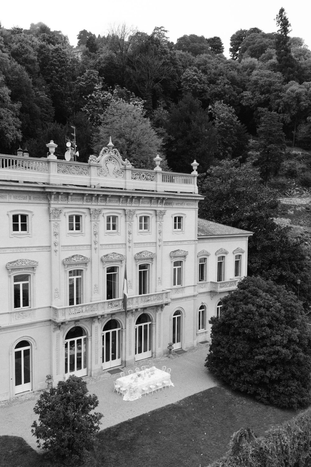 Grand white neoclassical villa with ornate balustrades and windows set against a lush hillside backdrop.