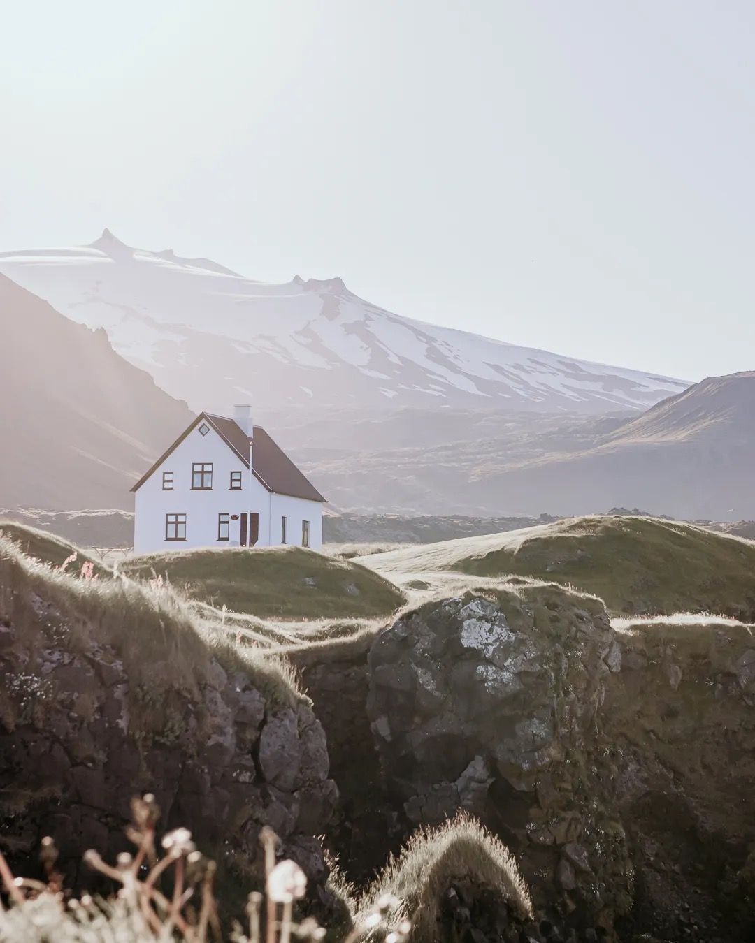 White house on a rugged Icelandic hillside with mountains in the background.