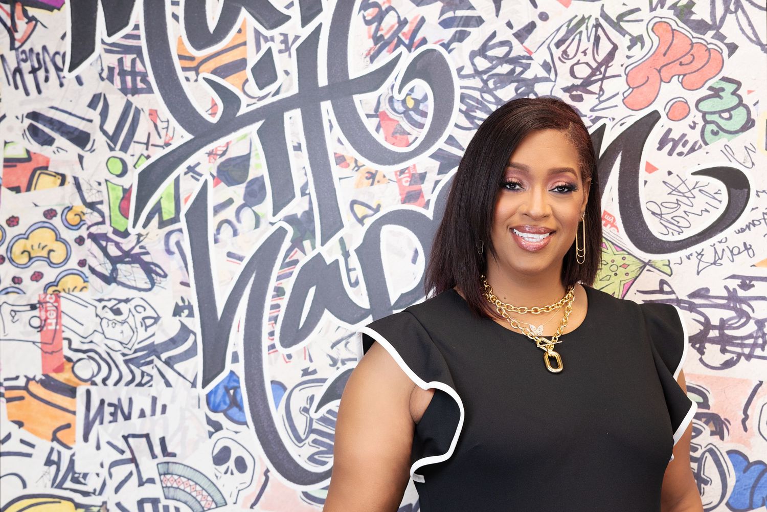 Professional portrait photo against a colorful graffiti wall background wearing a black top and statement earrings.