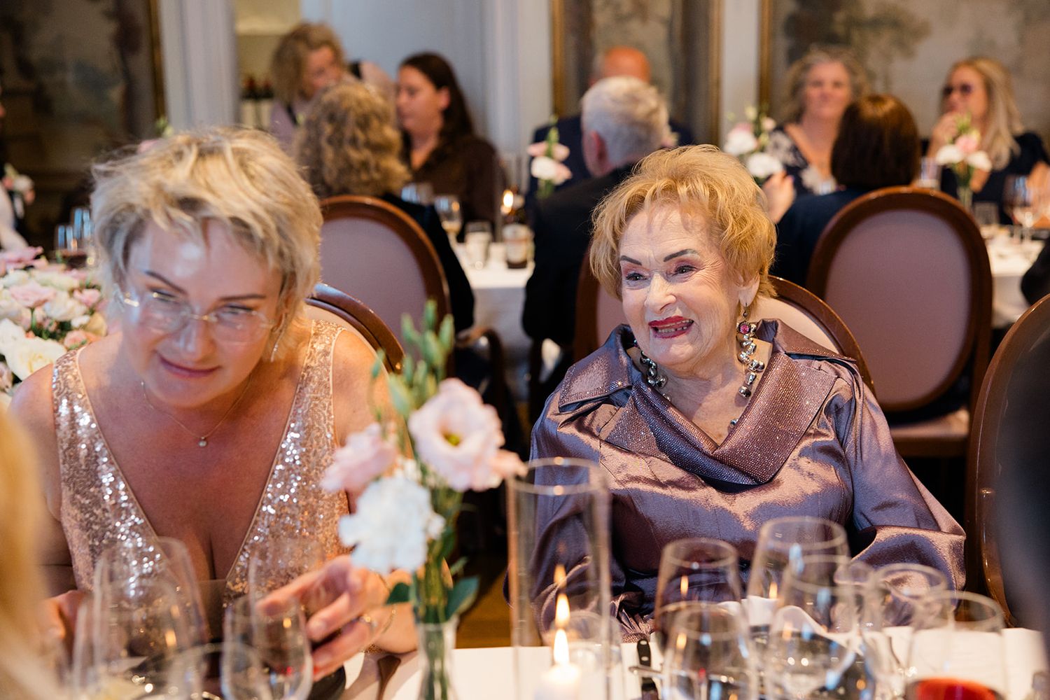 Guests laugh and share joyful moments around elegantly set dining tables at an indoor celebration event.