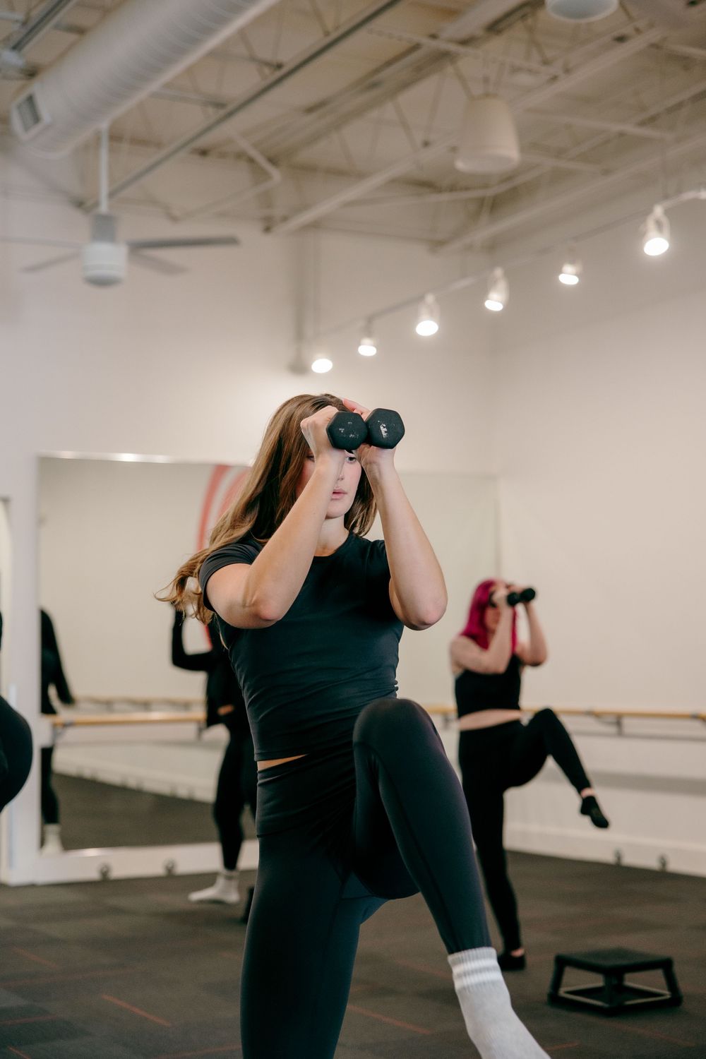 Person in black athletic wear performs stretching exercises in a bright studio space with track lighting.