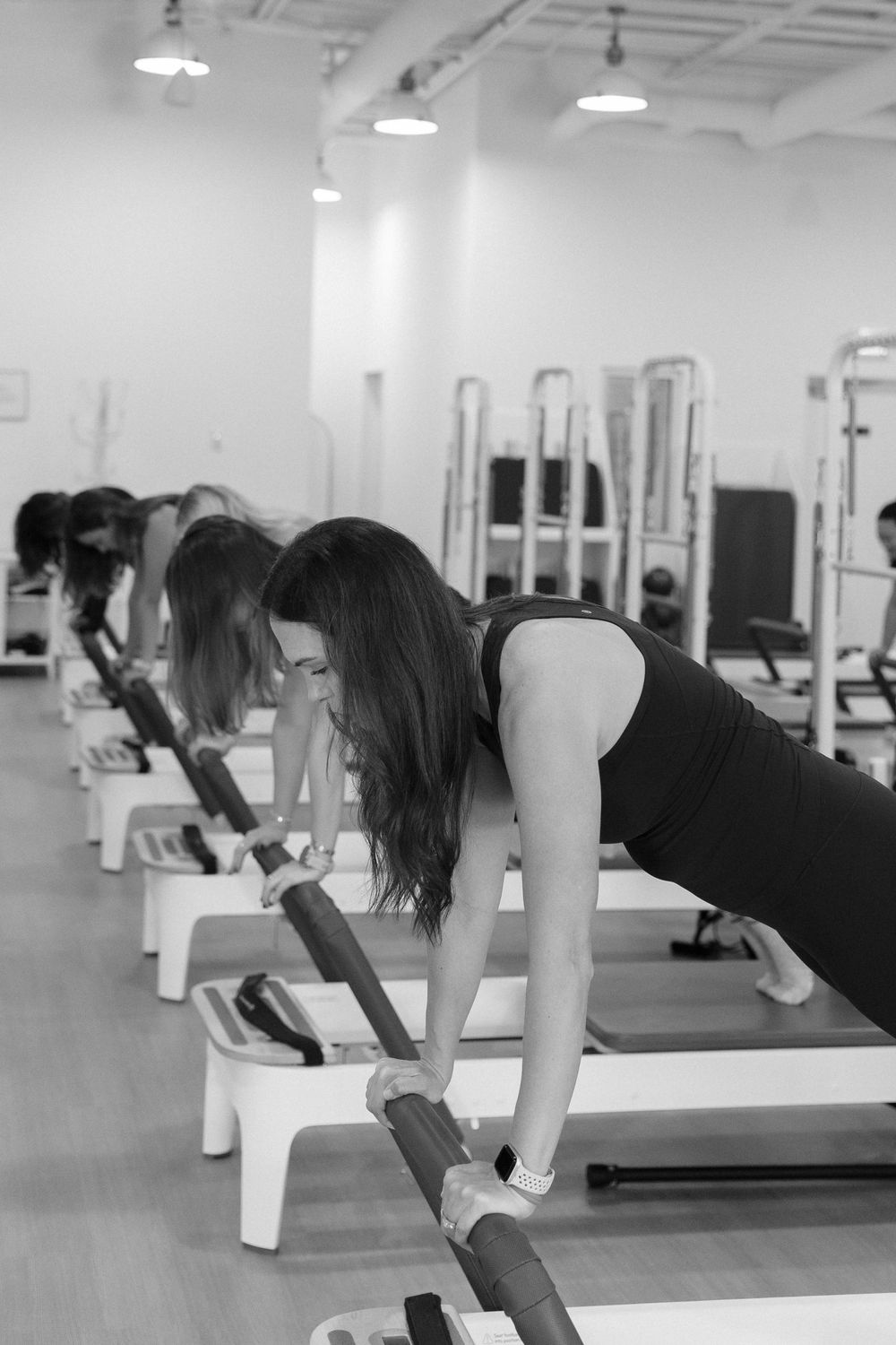 People practicing Pilates exercises on reformer machines in a bright, modern fitness studio.