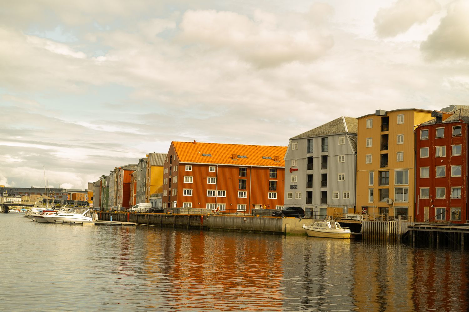 Row of colorful waterfront buildings reflected in calm harbor waters under cloudy skies.