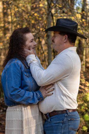 Couple sharing tender moment in fall woods, man in cowboy hat gently holding womans face, both smiling warmly.