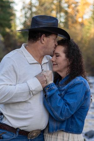 Couple sharing a tender kiss in autumn forest, man in cowboy hat and white shirt, woman in denim jacket.