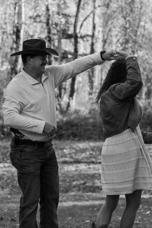Black and white photo of couple dancing outdoors, man in cowboy hat spinning woman in white dress.