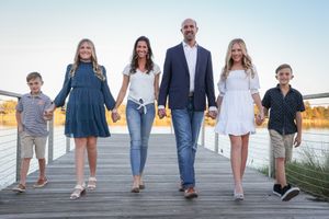 A family of five walks together on a wooden boardwalk at sunset near a waterfront.