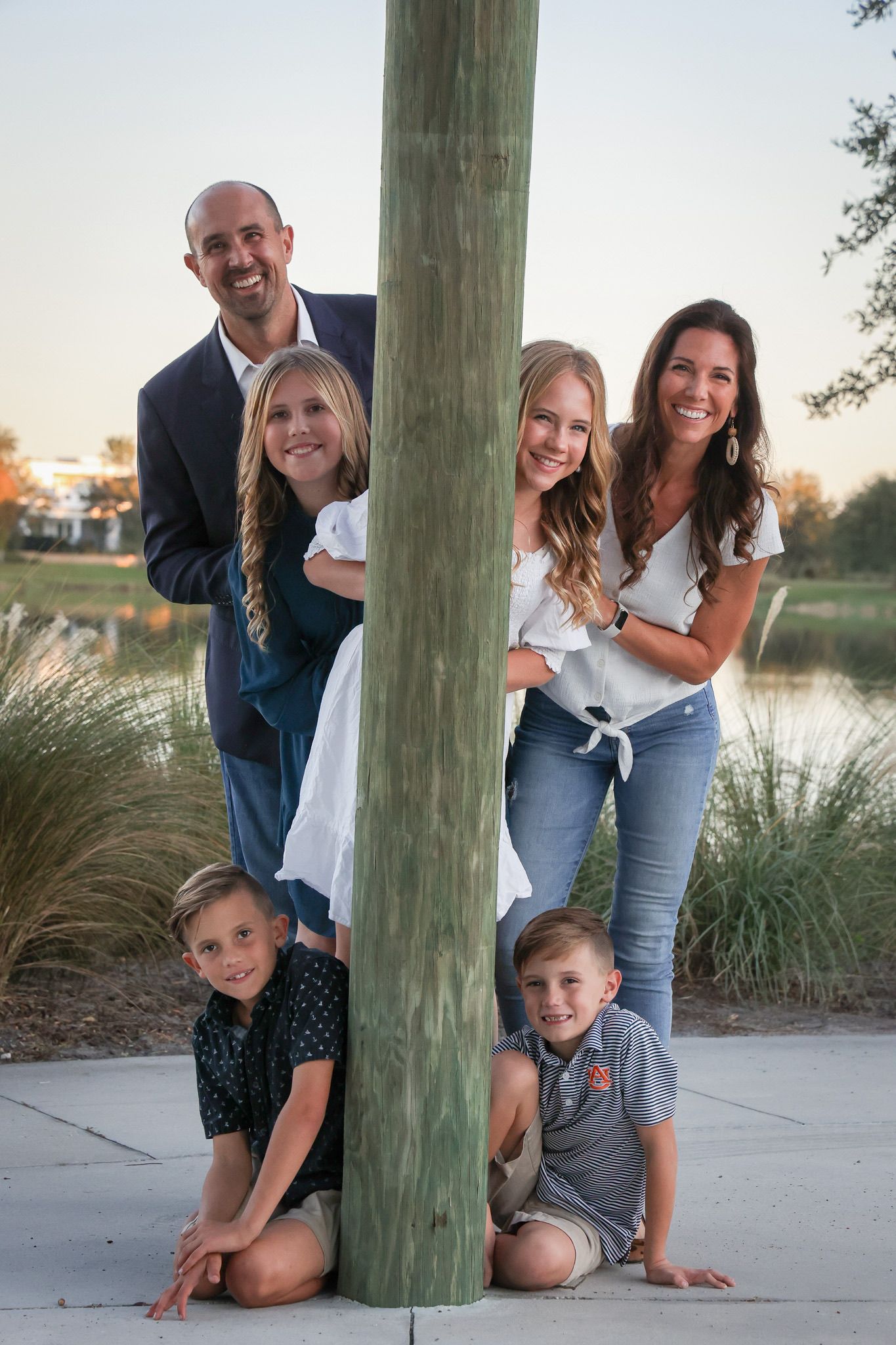 A playful family portrait arranged around a wooden pole outdoors at sunset.