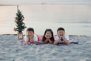 Family lying on beach sand with small Christmas tree at sunset.