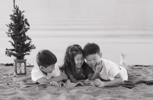 Black and white photo of family lying on beach with Christmas tree.