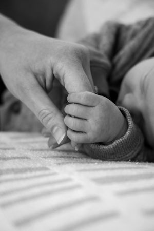 Close-up black and white image of adult and baby hands touching tenderly.