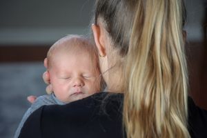 A sleeping newborn rests peacefully against a shoulder in soft lighting.