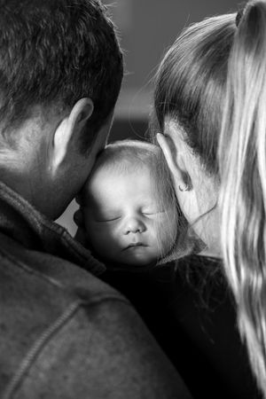 Black and white intimate portrait of a sleeping baby between two adults.