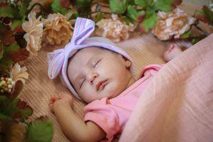 Sleeping baby wearing pink dress with floral decorations in a peaceful setting.