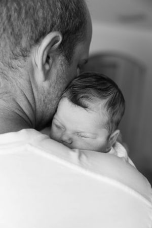 Black and white image of father holding sleeping newborn close.