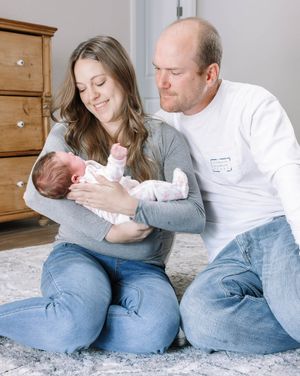 Family sitting together on carpet floor bonding with newborn baby.