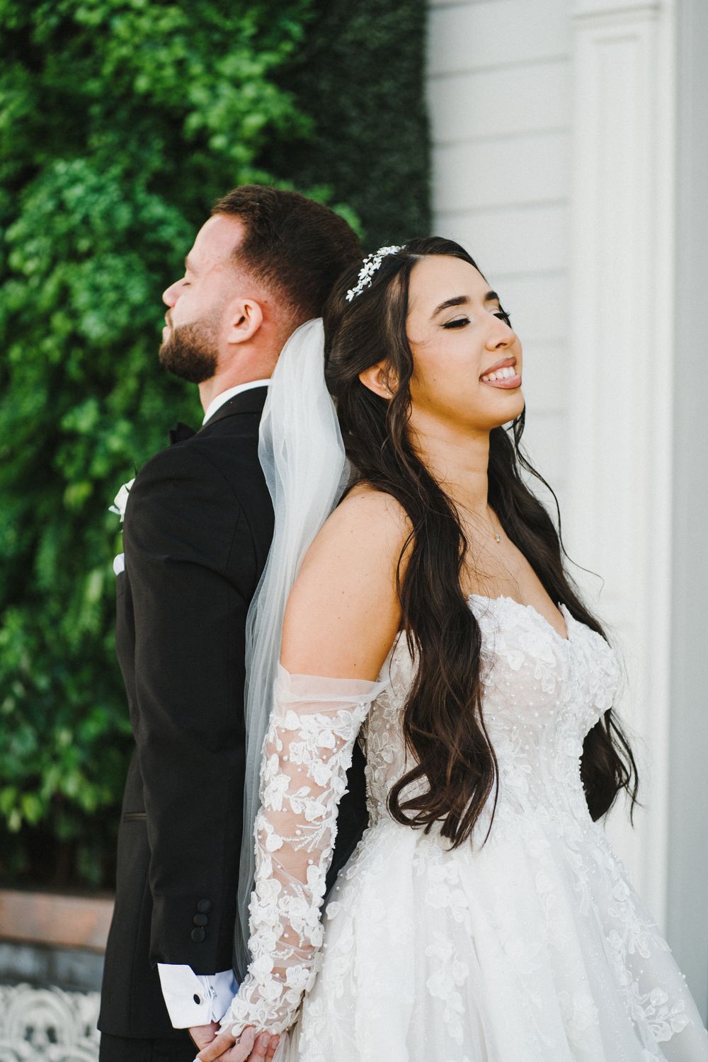 A bride and groom share joyful candid moments in front of white columns surrounded by lush greenery.