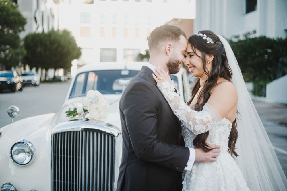 A wedding couple shares romantic moments in front of vintage Rolls Royce cars during their elegant photo session.