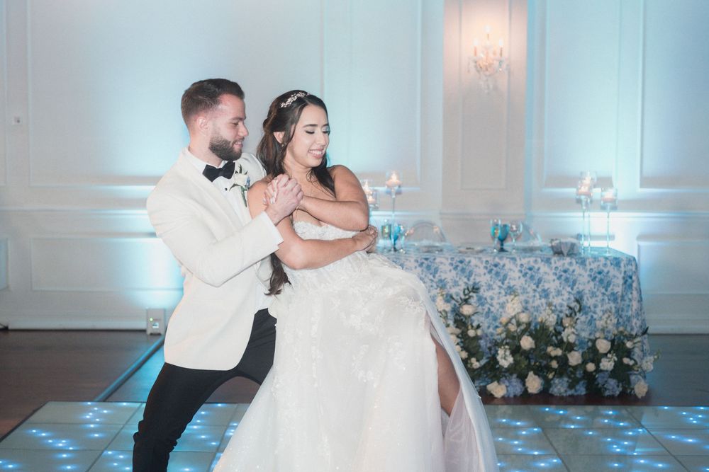 Bride and groom share their first dance at elegant wedding reception with floral backdrop and blue dance floor.