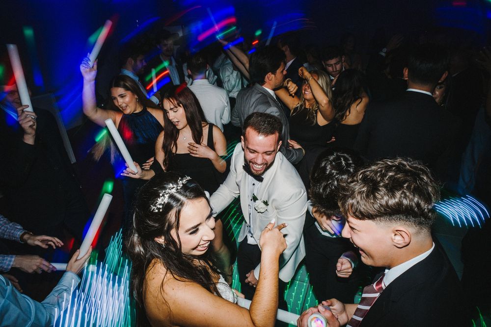 A crowd of people dancing and celebrating at a nightclub with colorful blue lighting and energetic atmosphere.