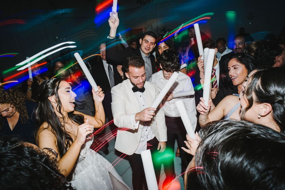 Party crowd dances and celebrates with glowsticks in a dark nightclub with colorful lights.