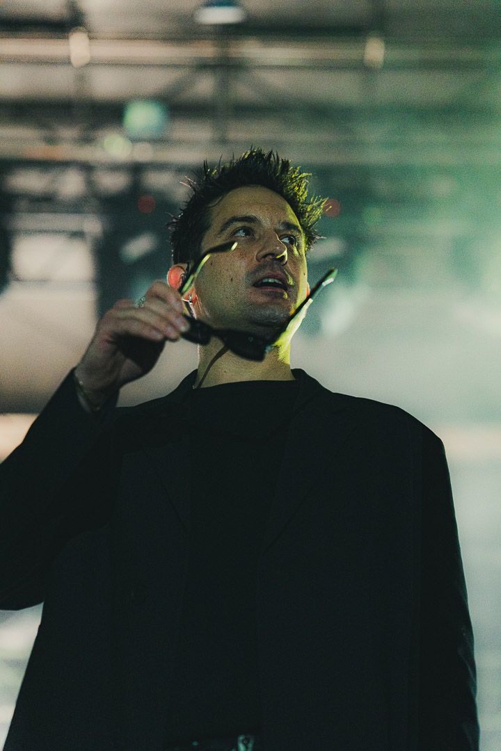 Performer in black clothing singing on stage with dramatic lighting and blurred background.