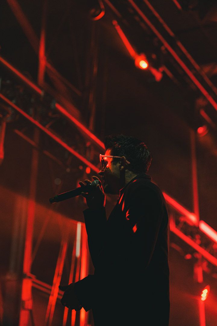 Silhouetted performer on stage with dramatic red lighting and beams creating an atmospheric concert environment.