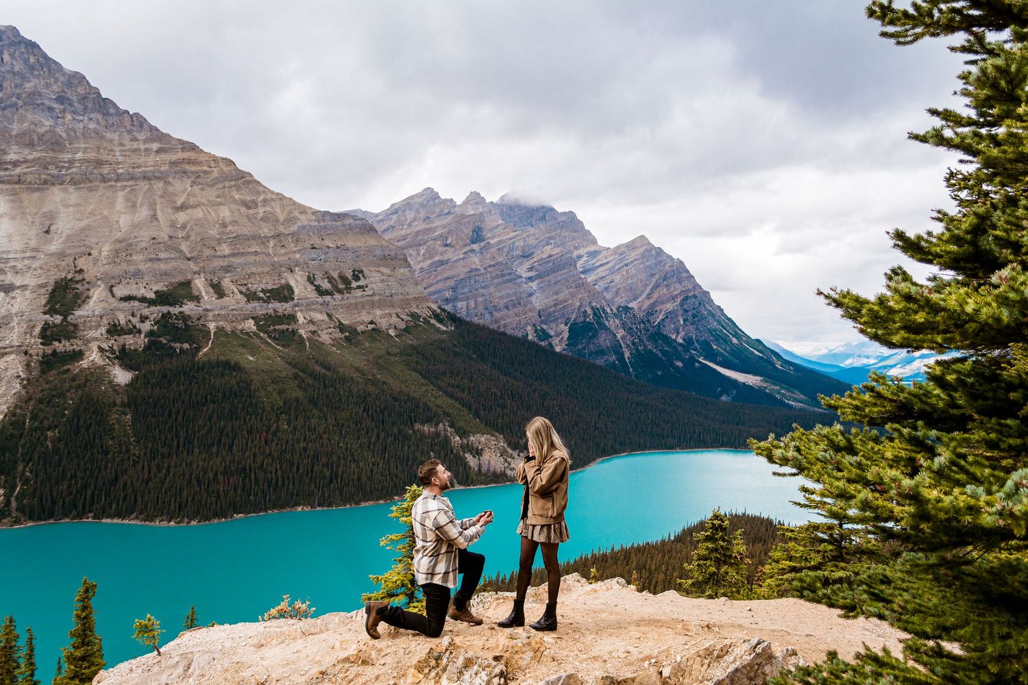 Hikers stand on a scenic mountain viewpoint overlooking turquoise Peyto Lake in Banff National Park, Canada.