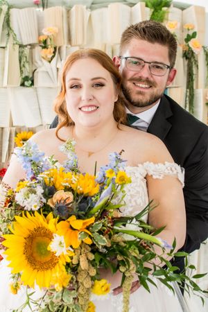 A joyful wedding photo featuring a bright sunflower bouquet with yellow and blue wildflowers against a white backdrop.