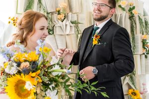 Wedding couple shares playful moment with sunflower decorations and white drapery backdrop.