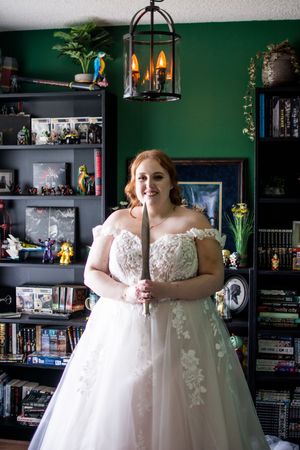 A white wedding gown with delicate lace details is shown against an emerald green wall with bookshelves.