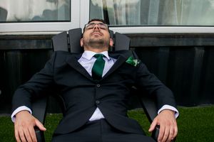 Wedding party members lounging on grass in formal attire.