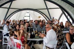 Wedding reception under a white tent with guests celebrating at decorated tables.