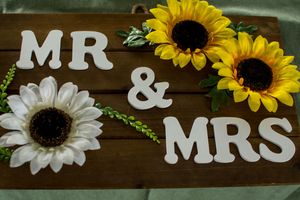 Rustic wooden sign with 'MR & MRS' text decorated with sunflowers.