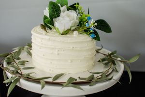 White wedding cake decorated with fresh greenery and flowers on a simple white plate.