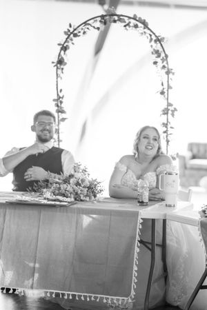 Wedding reception table setup with white linens and hanging floral decorations under a tent.