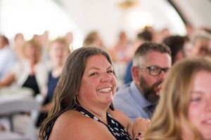 Wedding guests smile and laugh while seated during an outdoor celebration.