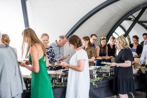 Wedding guests mingle and socialize under a large white tent at an outdoor reception.