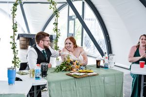 Reception venue decorated with greenery garlands and white tablecloths under arched ceiling.