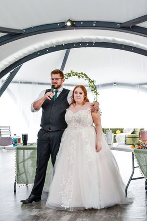 Wedding couple shares intimate moments under an elegant white tent with decorative floral arch.