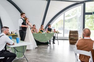 People gather in a modern curved glass building with white tent-like structures and industrial decor.