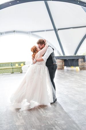 A couple shares a romantic dip during their wedding dance on a light-filled dance floor.