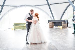 Bride and groom share their first dance on a polished white floor under a modern domed ceiling.