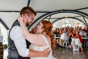 A couple shares a romantic dance together under a white tent during a wedding celebration.