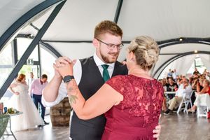 A couple shares a romantic dance moment during their wedding reception under a white tent.