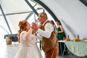 Wedding reception guests dancing and celebrating in a bright venue with curved ceiling.