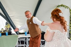 A couple dances joyfully together under a tent during their wedding celebration.