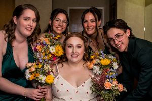 Wedding party members holding vibrant yellow and orange bouquets while gathered for a group photo.