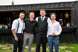 Wedding party in formal attire poses together outside a dark building with string lights.